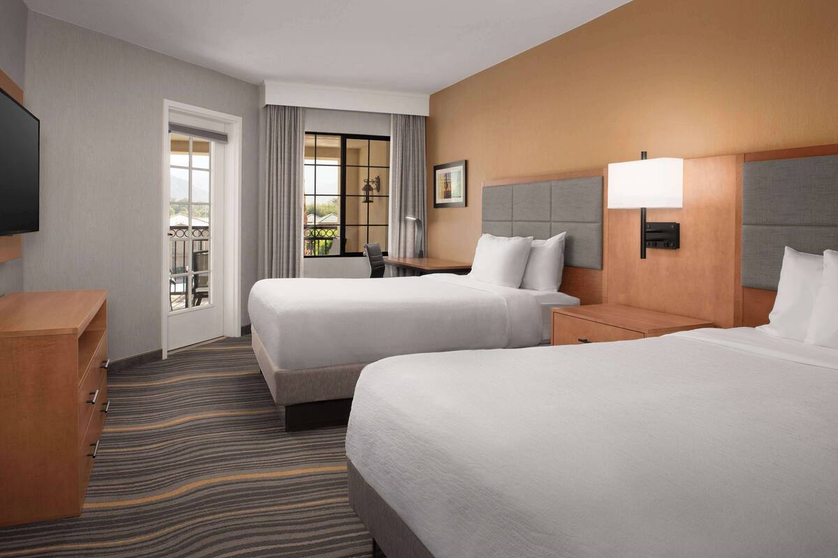 Une chambre d’hôtel avec deux lits, un bureau, une chaise, une télévision et une vue sur l’extérieur.