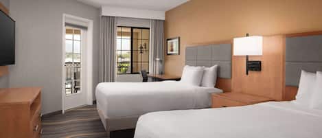Habitación de hotel con dos camas, un escritorio, una silla, un televisor y vista al exterior.