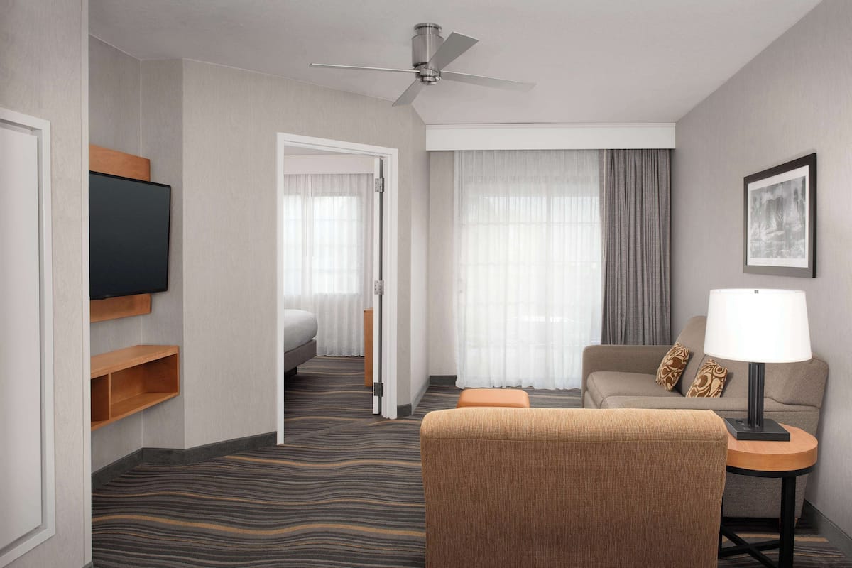 Une chambre d’hôtel équipée d’un lit, d’un canapé, d’une chaise, d’une télévision, d’une lampe et d’un ventilateur de plafond.