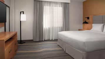 A hotel room with a large bed, a desk with drawers, a standing lamp, and a window with curtains.
