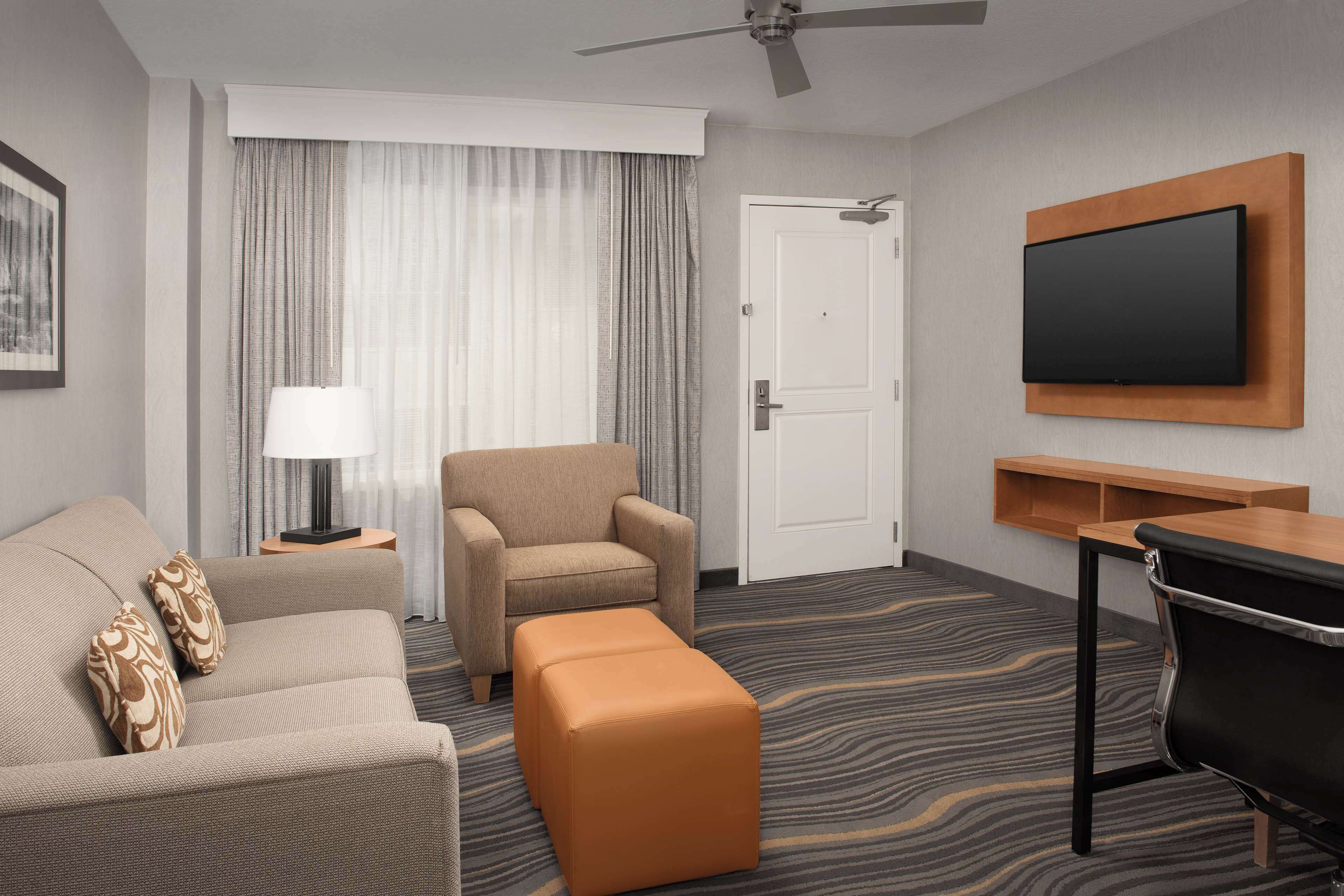 Ein Hotelzimmer mit Sofa, Ohrensessel, Hocker, Fernseher und Schreibtisch.