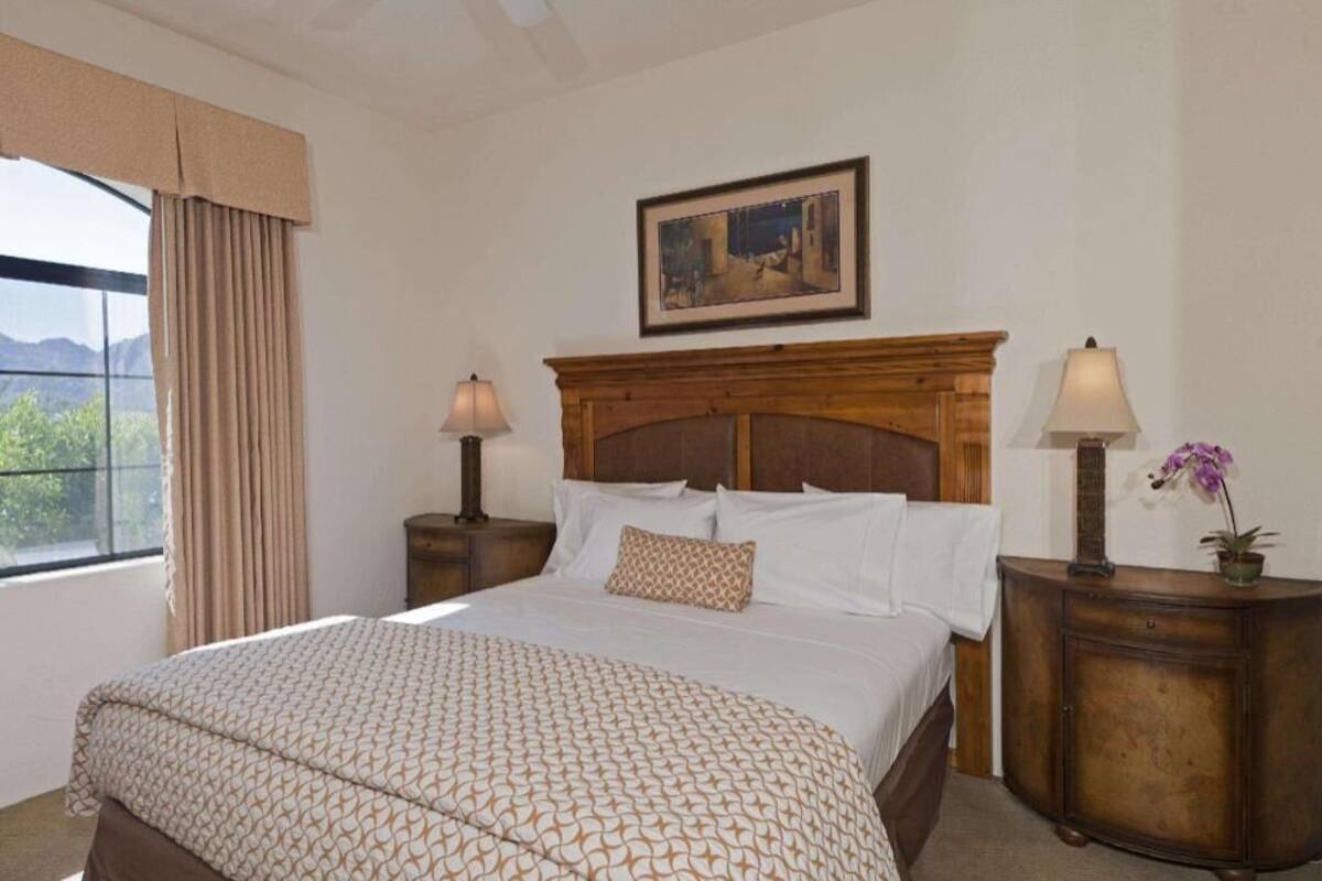 Une chambre d’hôtel avec un grand lit, deux tables de chevet avec des lampes, un tableau au-dessus du lit et une fenêtre avec des rideaux.