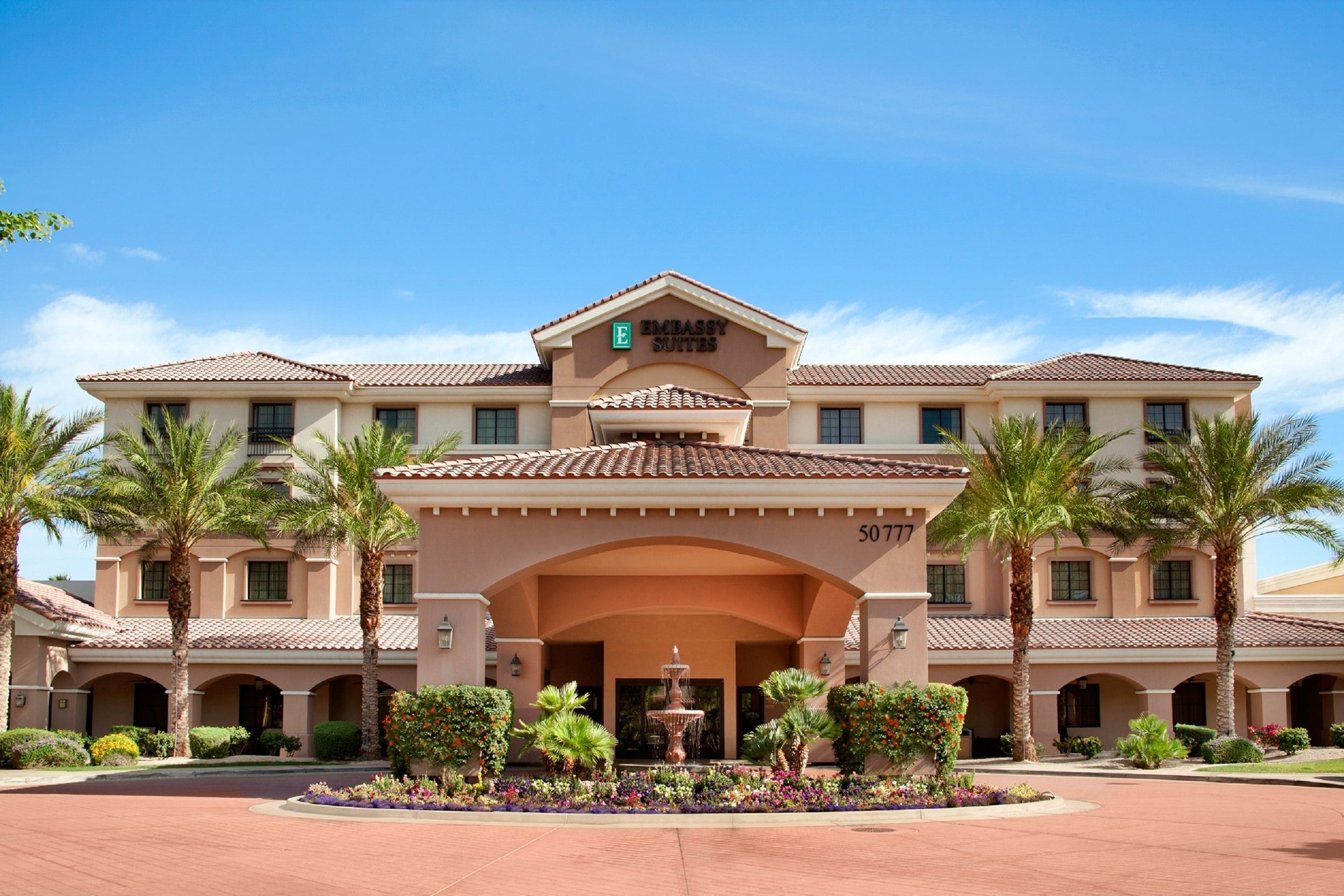 A large, multi-story hotel with a central courtyard, palm trees, and a fountain.