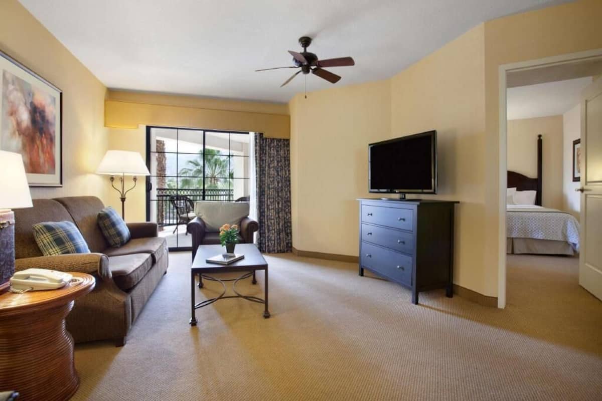 Une chambre d’hôtel équipée d’un canapé, d’une table basse, d’une télévision, d’un bureau et offrant une vue sur le balcon.