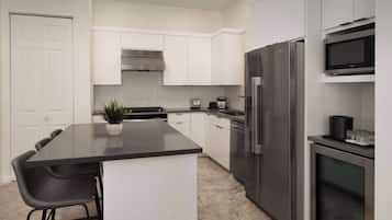 Una cocina moderna con armarios blancos, un refrigerador de acero inoxidable, un microondas empotrado y una pequeña isla con taburetes de bar.