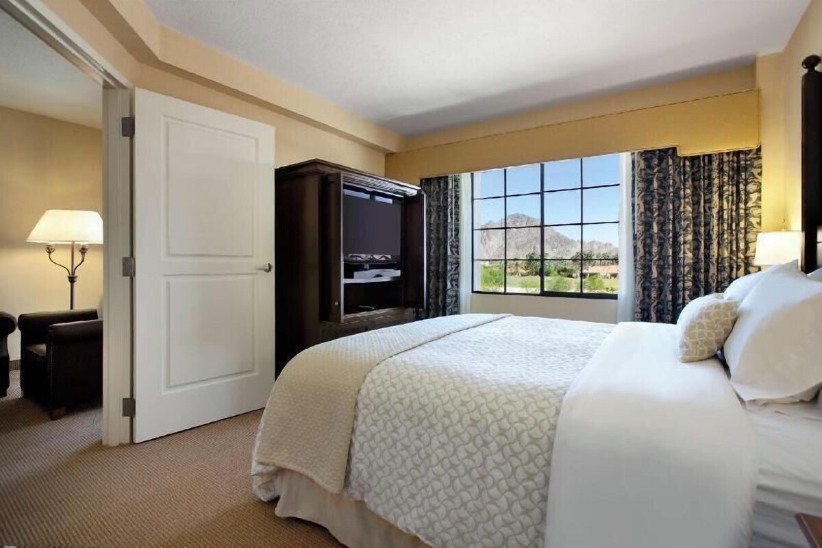 A hotel room with a bed, a TV, a desk, and a window with a view.