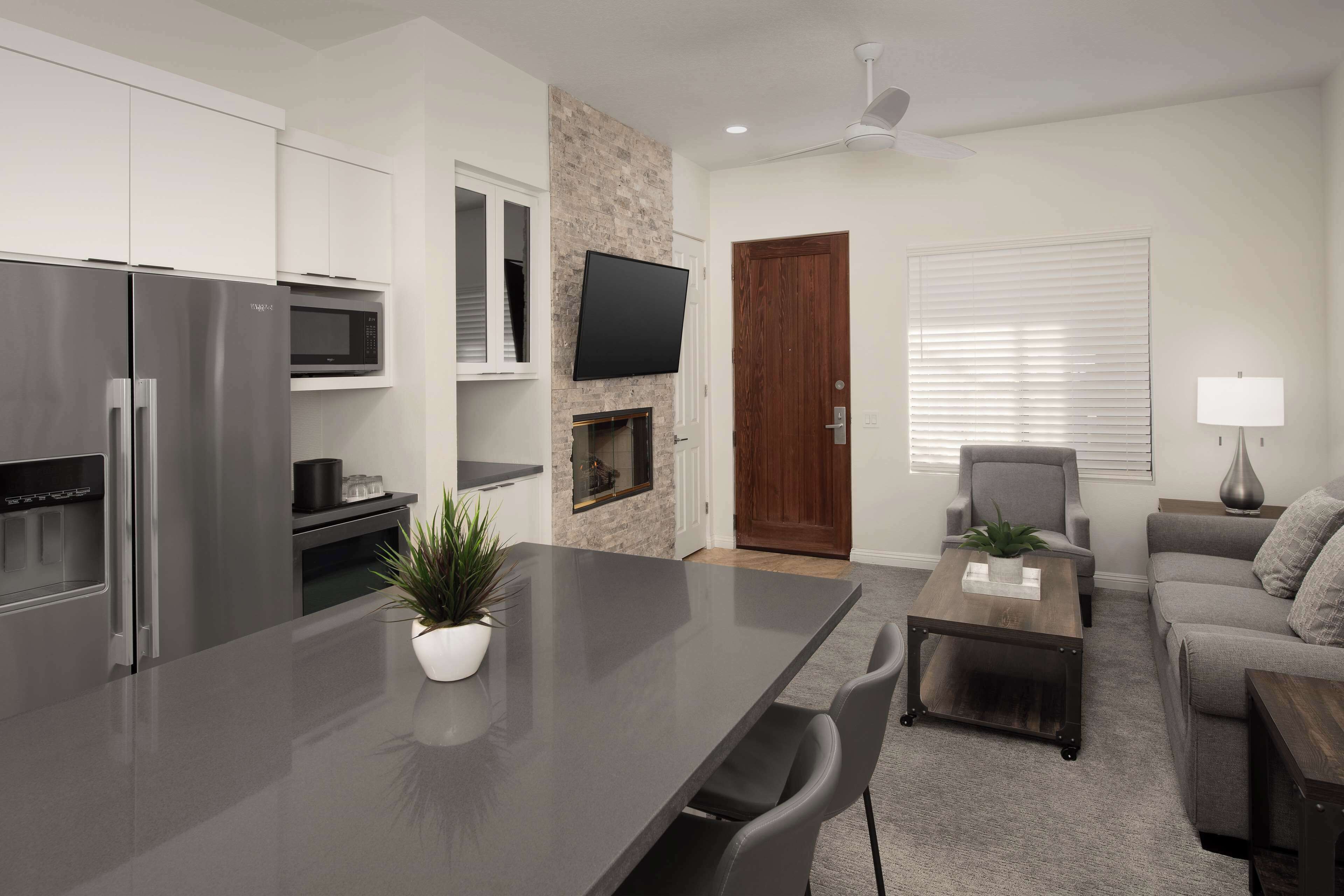 A modern kitchen with stainless steel appliances, a flat-screen TV, and a stone accent wall.