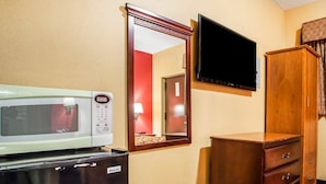 Ein Hotelzimmer mit einer Mikrowelle, einem Fernseher, einer Holzkommode und einem Spiegel.