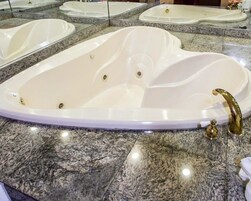 Una bañera grande y ovalada con grifo dorado en un baño con encimeras de granito y varios espejos.
