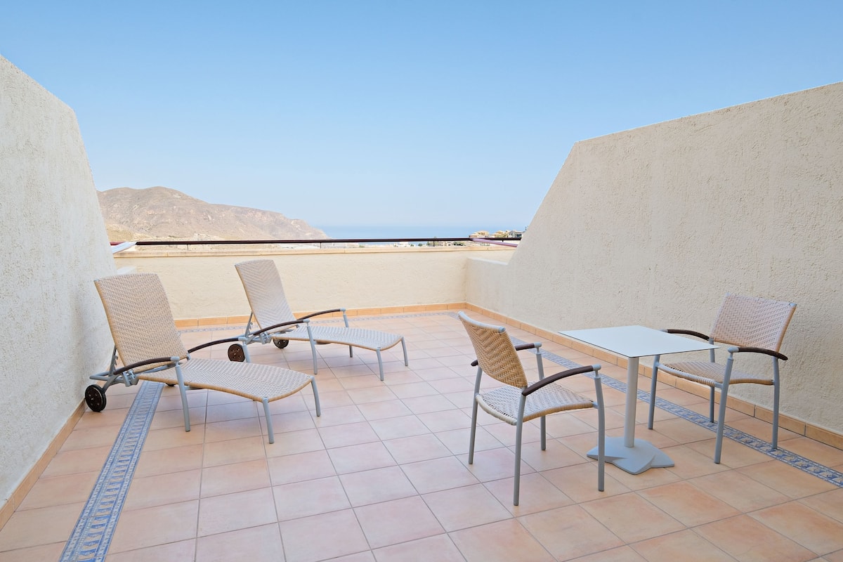 A terrace with four chairs and a table, a tiled floor, and a view of the sea and mountains.