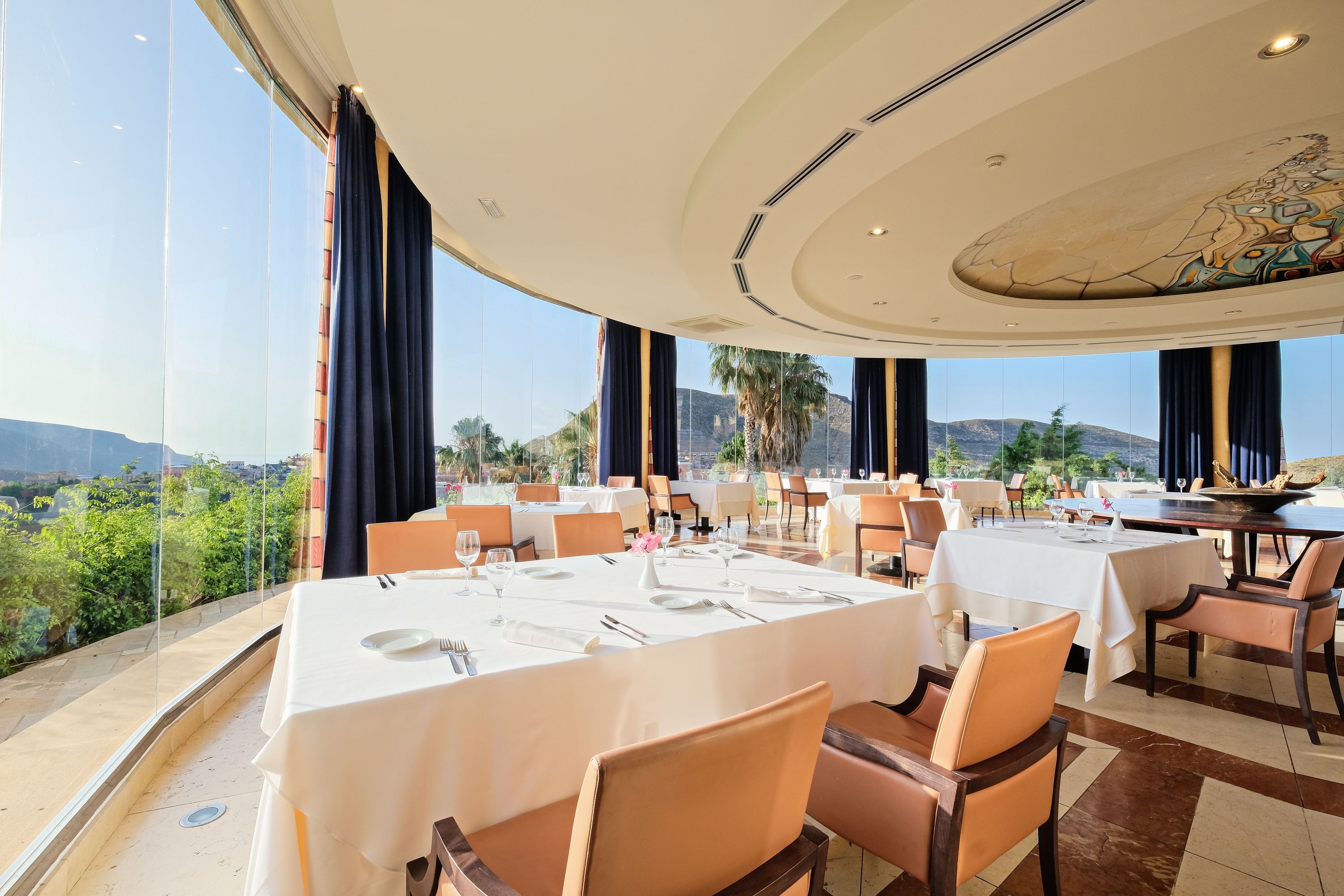 A restaurant with tables set for dining, large windows, and a view of the landscape.