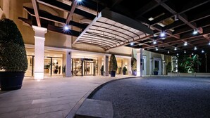An outdoor area with a curved pathway leading to a building entrance, potted plants, and a covered walkway with a metal roof.