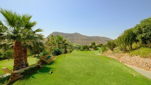 A well-maintained golf course with a clear view of a mountain in the background, surrounded by lush greenery and palm trees.