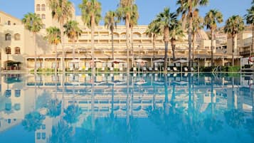 Un hôtel avec une piscine, des palmiers et un ciel bleu azur.