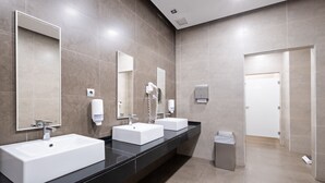A modern bathroom with two sinks, a mirror, a hand dryer, and a trash bin.