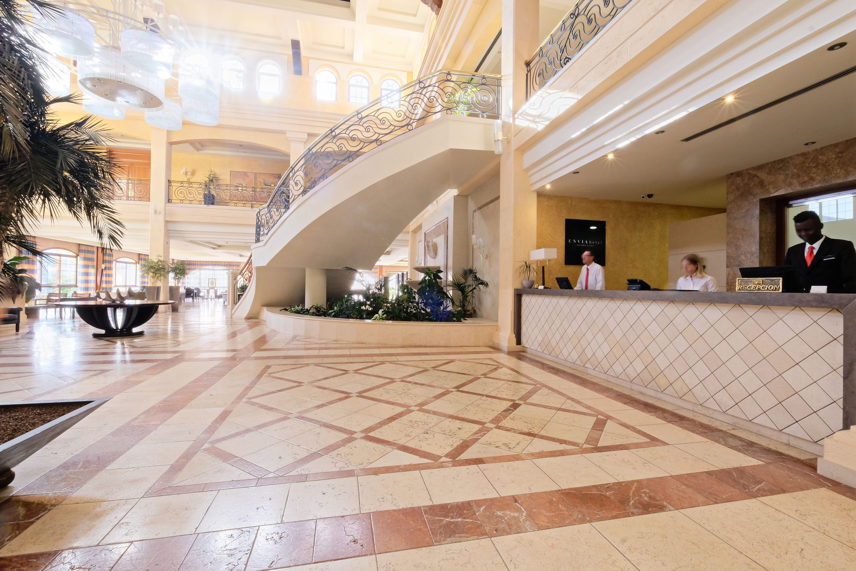 A spacious lobby with a reception desk, a decorative railing, and a tiled floor.