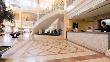 A spacious lobby with a reception desk, a decorative railing, and a tiled floor.
