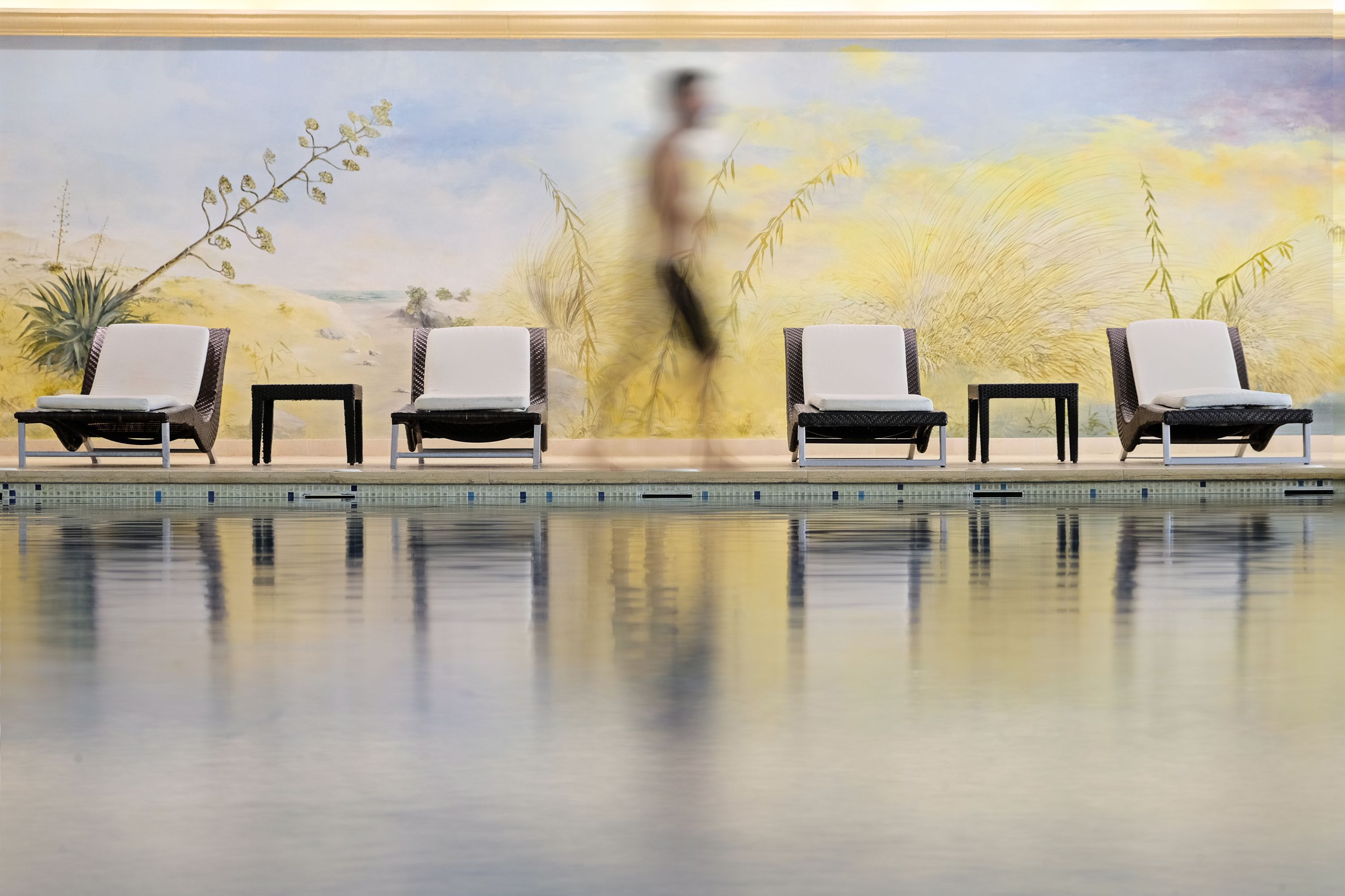 A pool area with lounge chairs and a mural of a desert landscape.