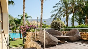 Eine Holzterrasse mit Korbmöbeln, eine Steinmauer und ein Pool im Hintergrund.