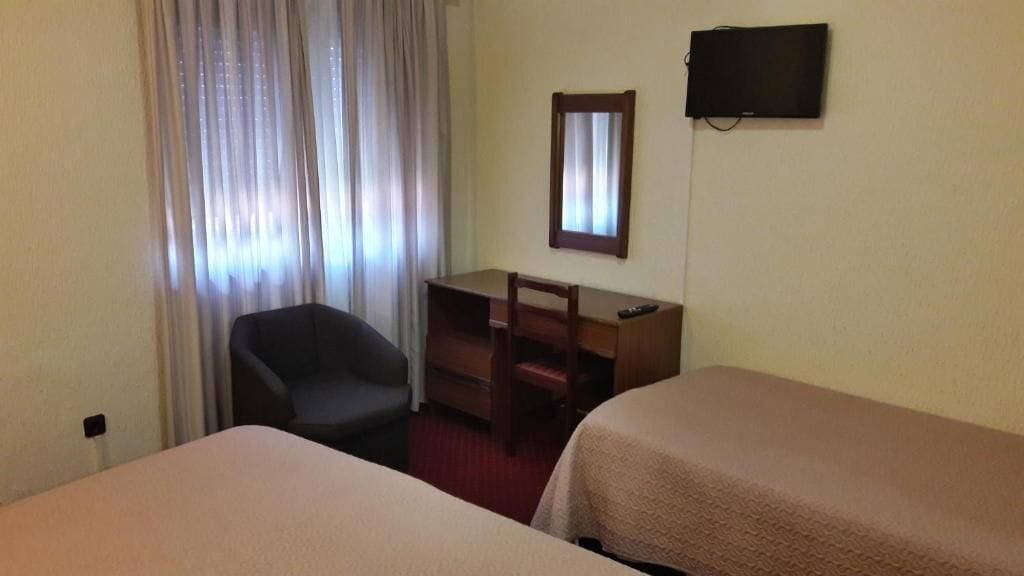 Une chambre d’hôtel avec deux lits, un bureau, une chaise, une télévision et une fenêtre avec des rideaux.