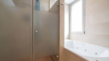 Een moderne badkamer met een douchecabine van glas, een wit bad en een raam voor natuurlijk licht.