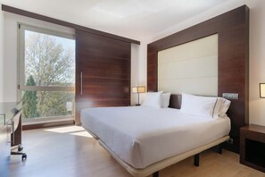 A modern hotel room with a large bed, a desk, and a view of trees through a large window. - Eurostars i-Hotel (Pozuelo de Alarcon)