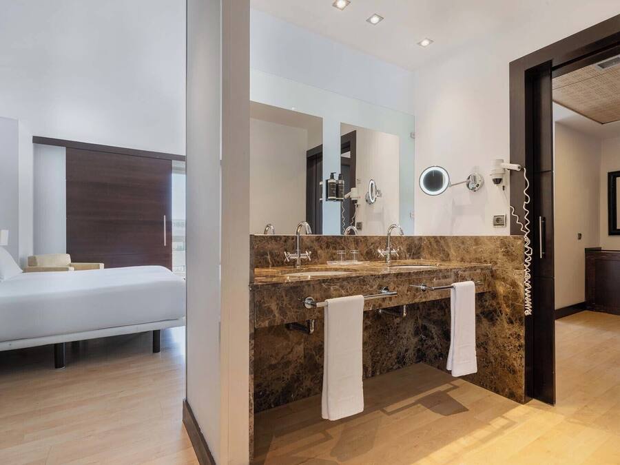 Una habitación de hotel moderna con una cama, un tocador de mármol con lavabo y un espejo grande.