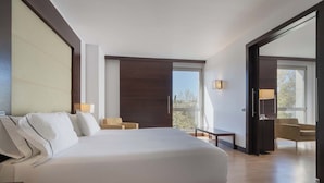 A hotel room with a large bed, a small table, two chairs, a balcony with a view, and a sliding door. - Eurostars i-Hotel (Pozuelo de Alarcon)