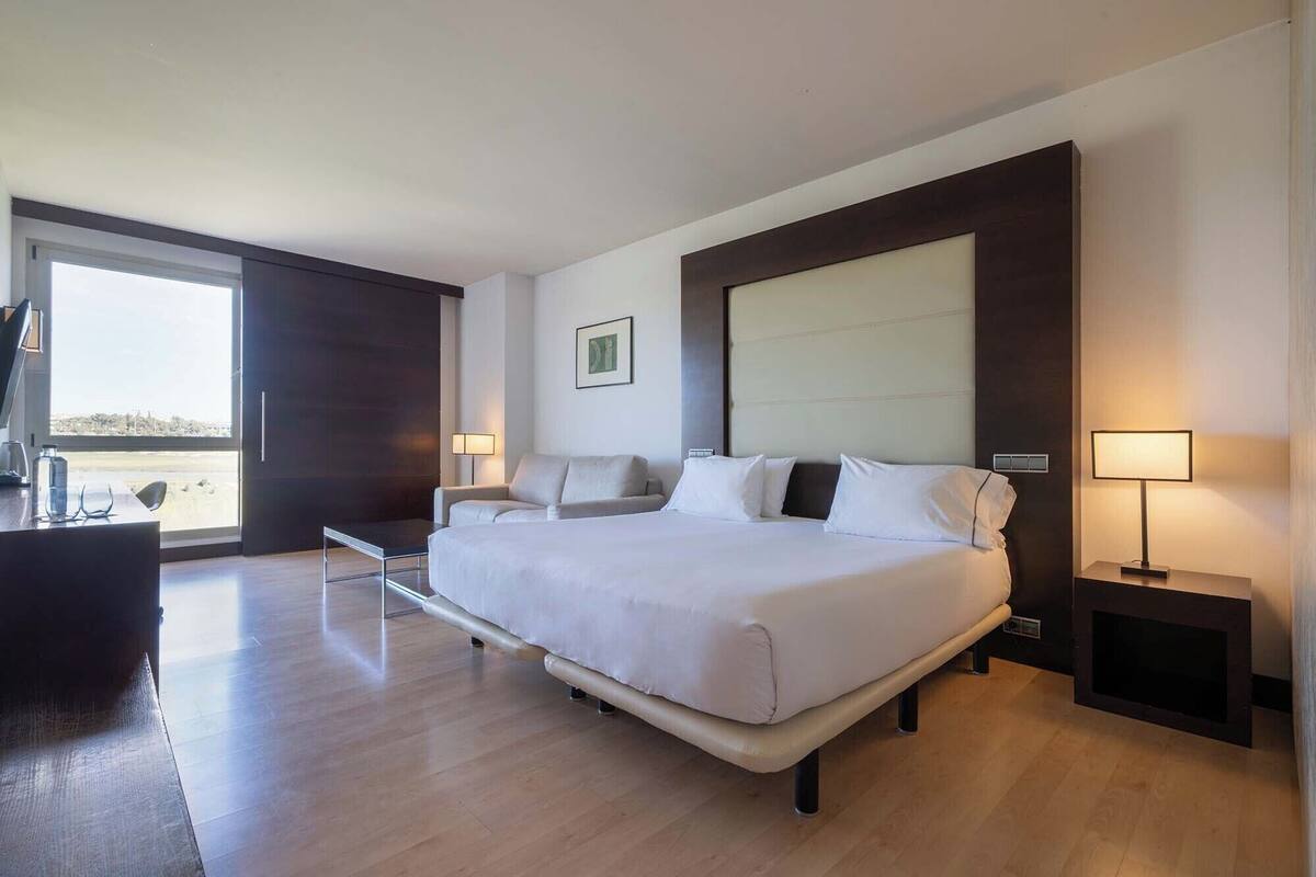 A modern hotel room with a large bed, a desk, and a view of the outdoors.