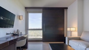 A hotel room with a desk, chair, sofa, TV, and a view of the city. - Eurostars i-Hotel (Pozuelo de Alarcon)