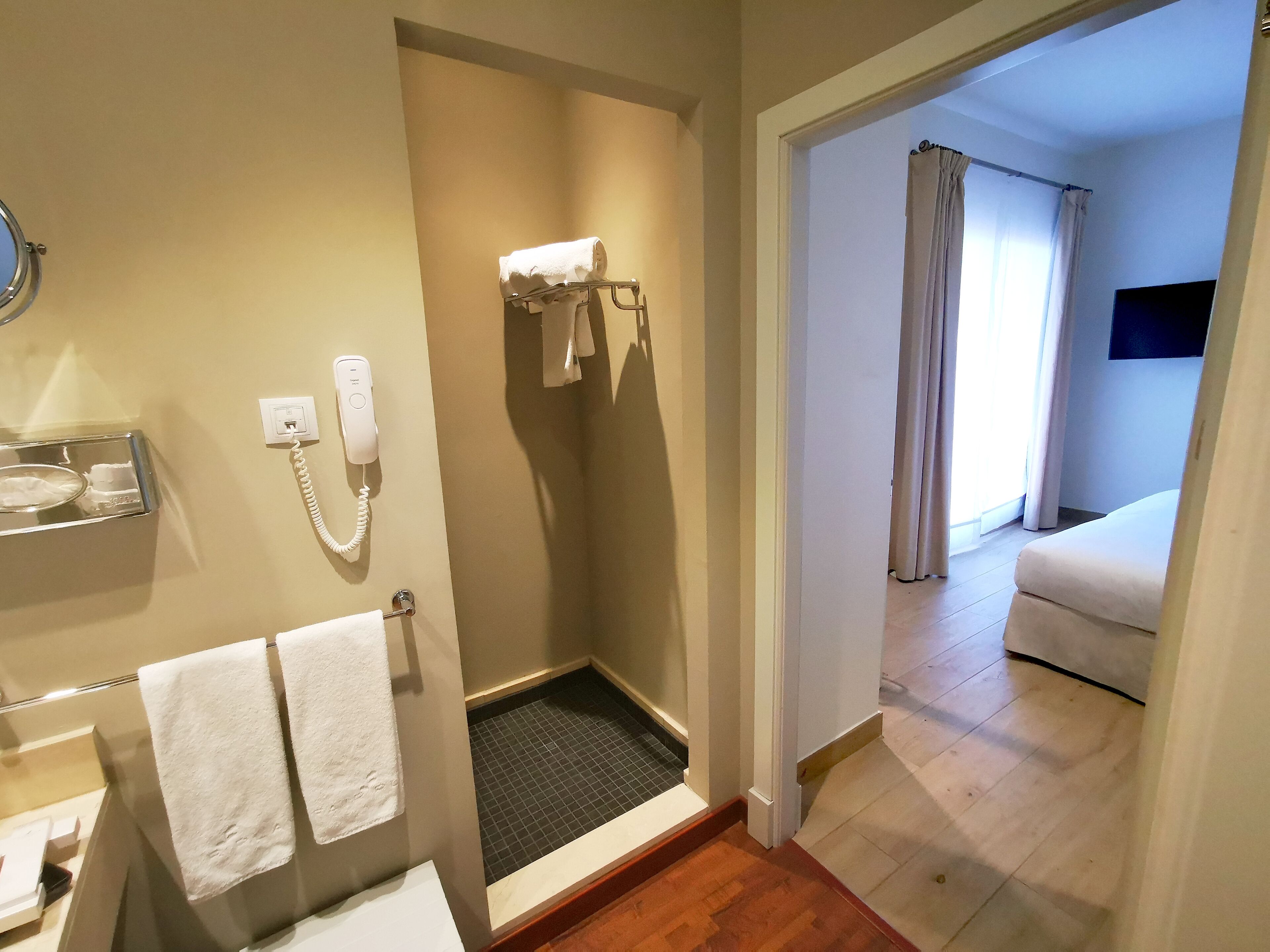 Un baño de hotel con ducha, inodoro y lavamanos. Hay un teléfono en la pared y un perchero con toallas.