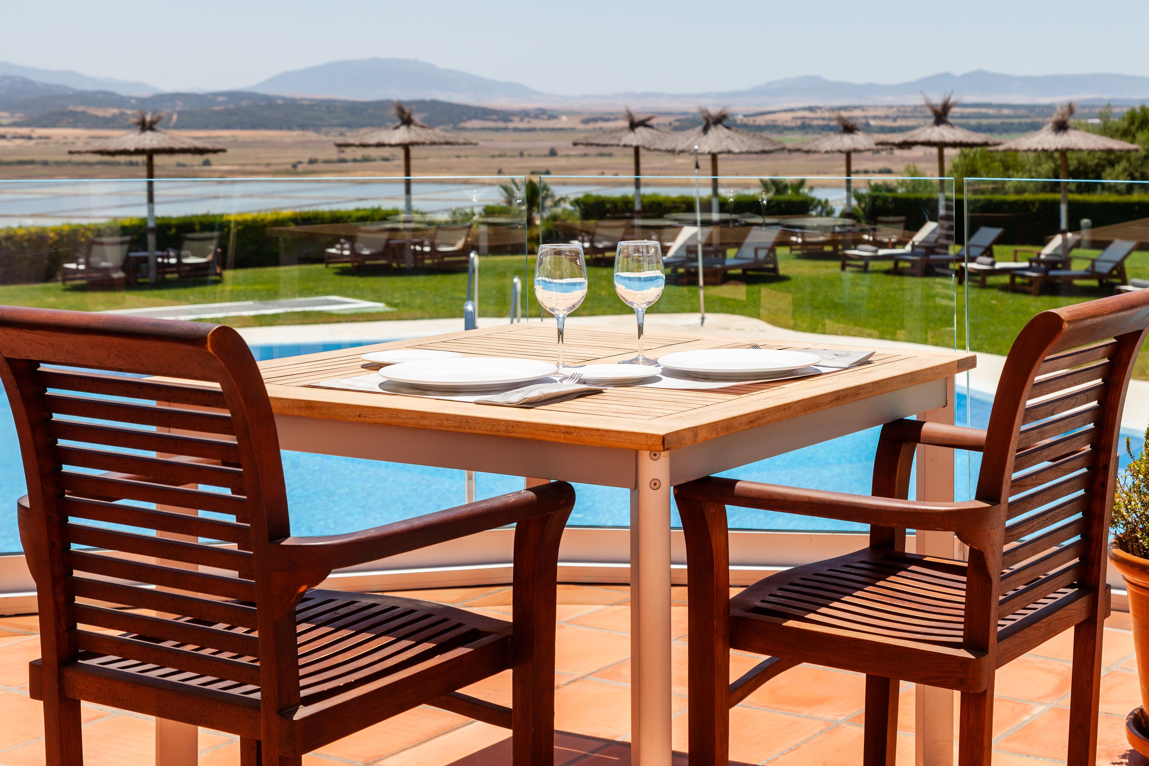 A table set for two with a view of a pool and mountains in the background.