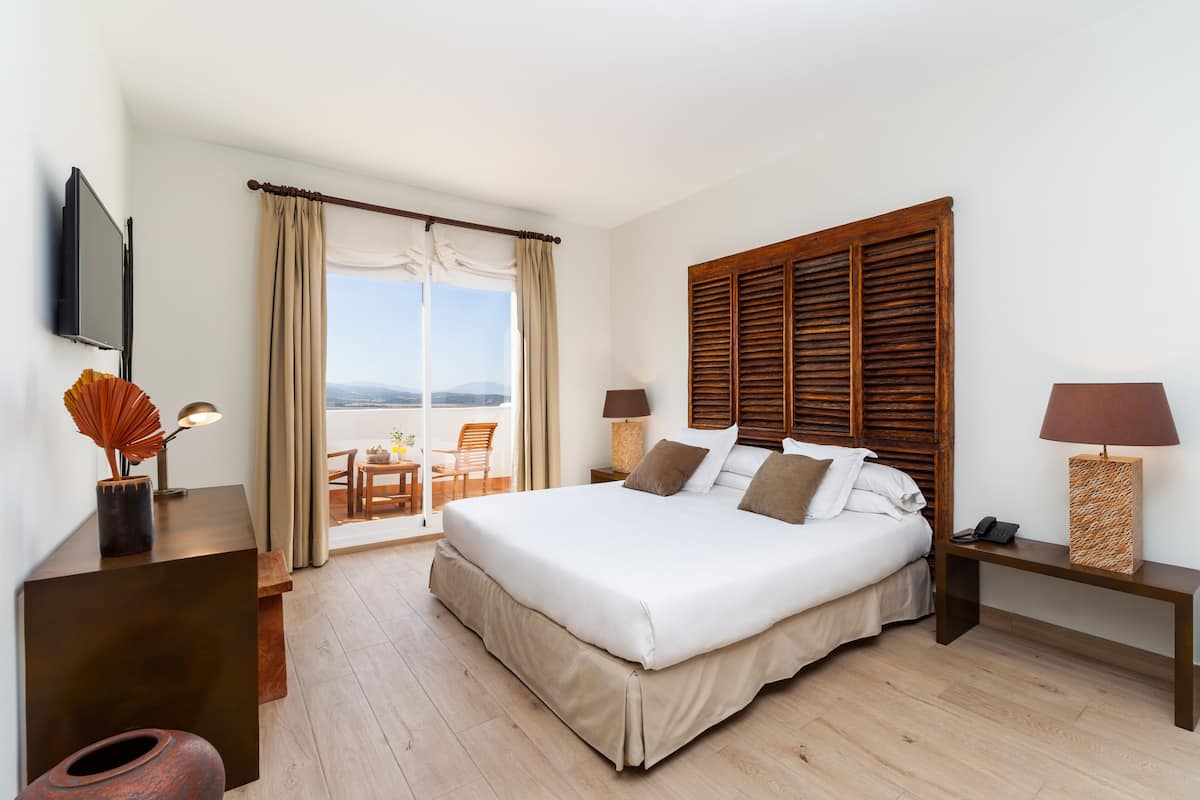 Ein Hotelzimmer mit einem großen Bett, einem Fernseher, einem Schreibtisch und einem Balkon mit Blick.