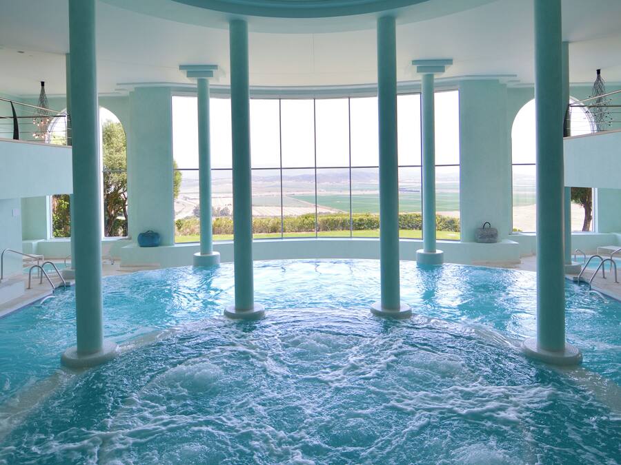 Una piscina interior con vistas despejadas al exterior, rodeada de columnas y un techo alto.
