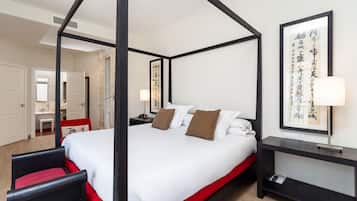 Una habitación de hotel moderna con cama con dosel, una mesita de noche con lámpara y una obra de arte grande enmarcada en la pared.