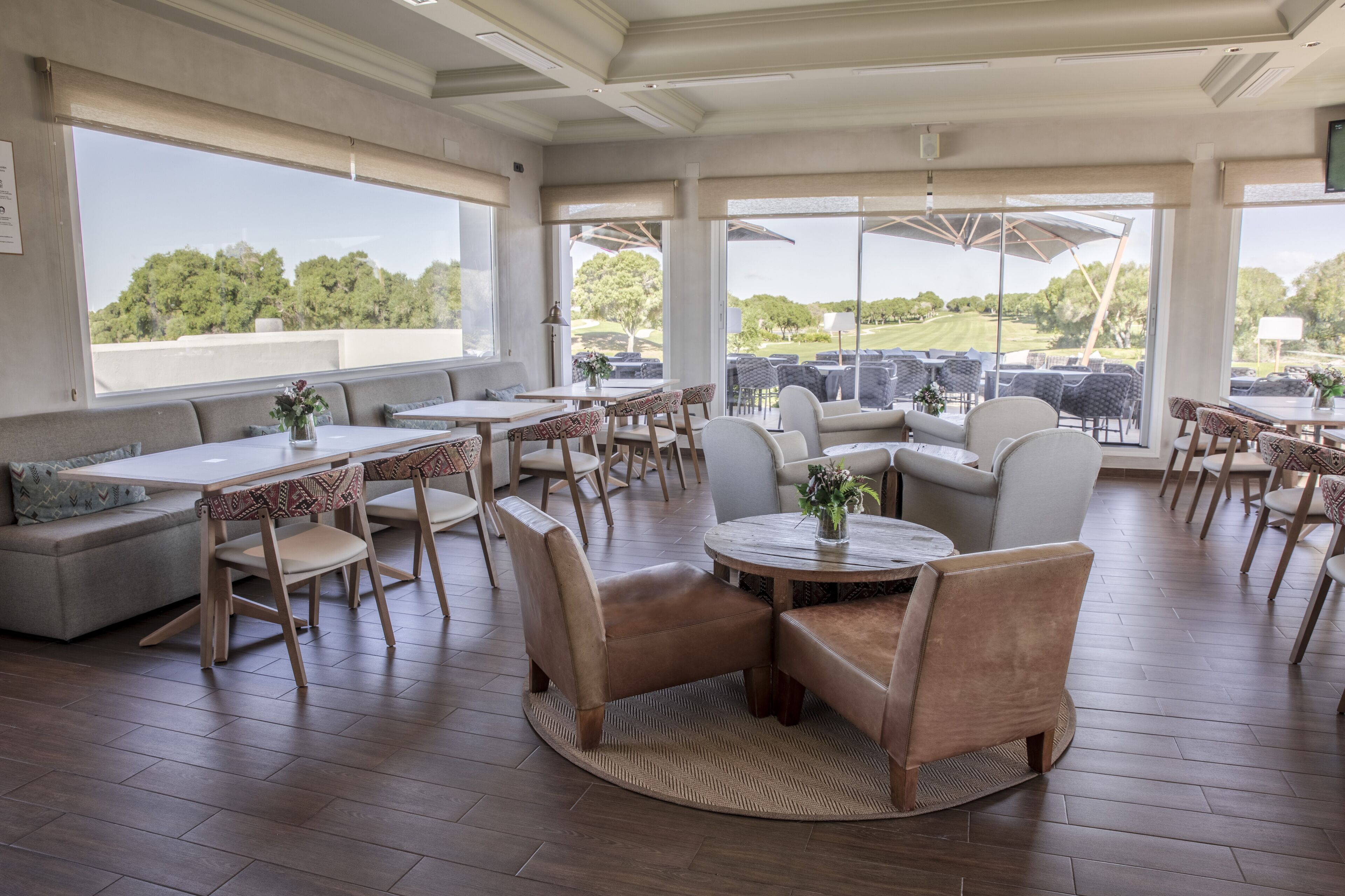 A spacious outdoor dining area with multiple tables and chairs, large windows offering a view of the surrounding landscape.