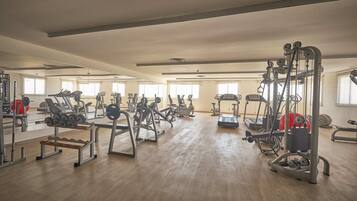 Une salle de sport spacieuse, équipée de divers appareils d’exercice, de miroirs et bénéficiant d’un éclairage naturel abondant.