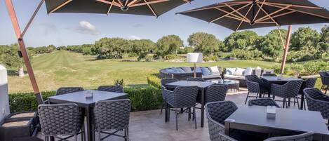 Une terrasse extérieure avec des tables et des chaises, de grands parasols et une vue sur un terrain de golf.