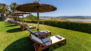 A row of wooden lounge chairs with thatched umbrellas, arranged on a well-manicured lawn with a view of a beach and distant hills. - Hotel Fairplay Golf & Spa Resort-by Grupo Tribu (Benalup-Casas Vieja)