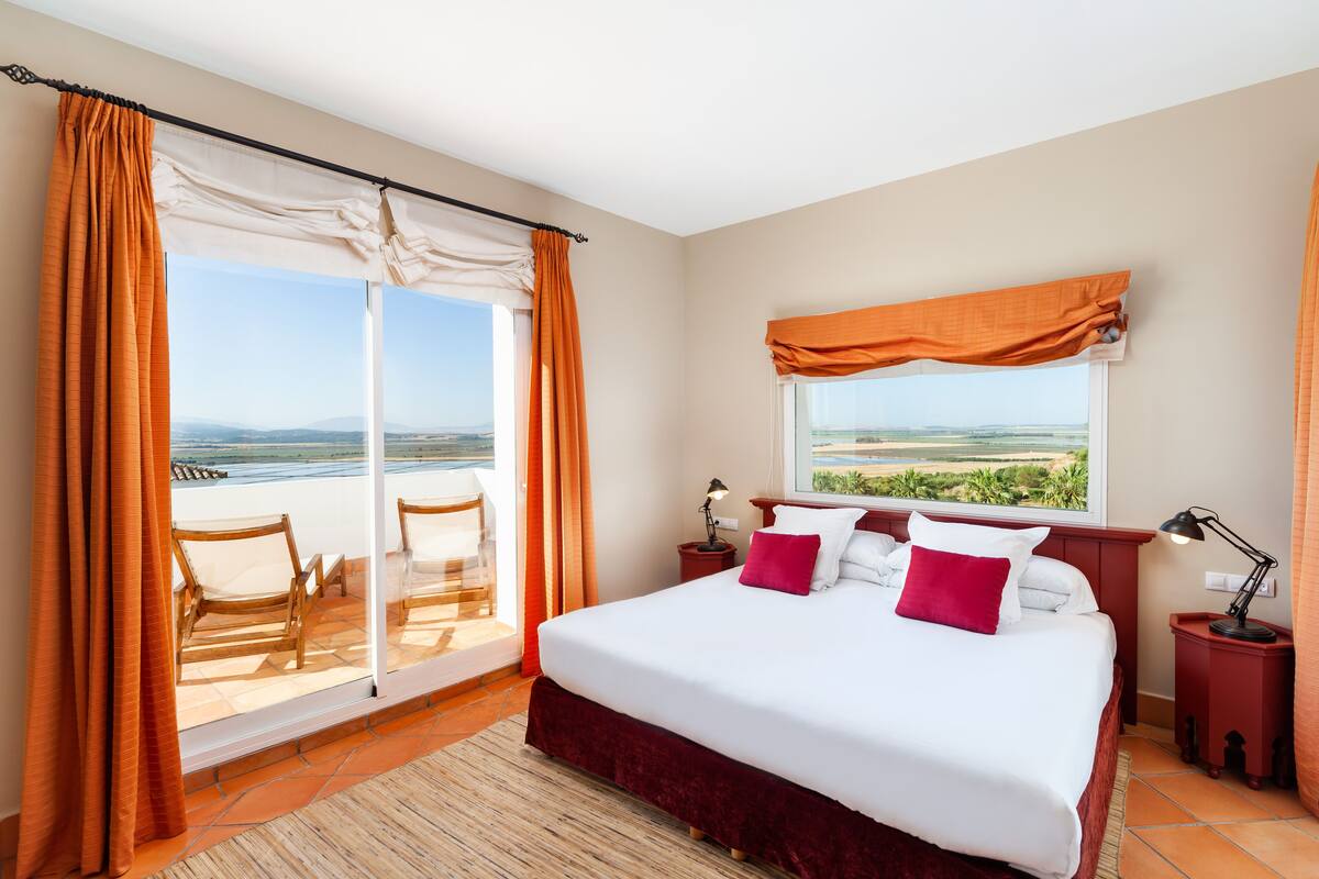Ein Schlafzimmer mit einem großen Bett, Blick ins Freie und einem Balkon mit Sitzgelegenheiten.