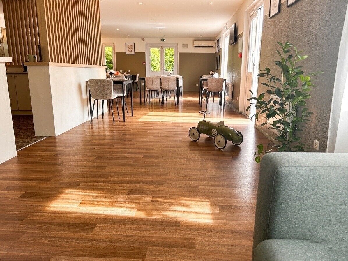 A spacious room with a wooden floor, a dining area with chairs, a small table, and a green toy car.
