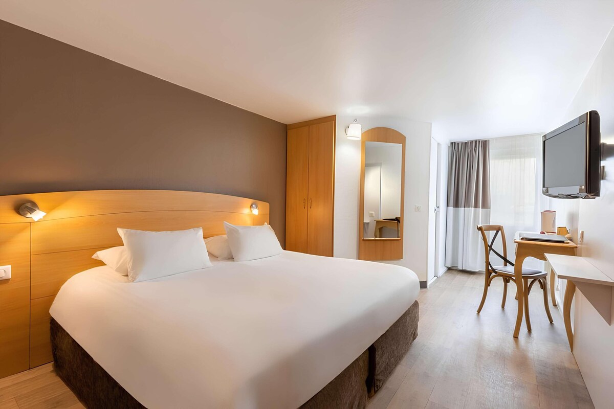 Ein Hotelzimmer mit einem großen Bett, einem Schreibtisch, einem Sessel, einem Fernseher und einem Spiegel.