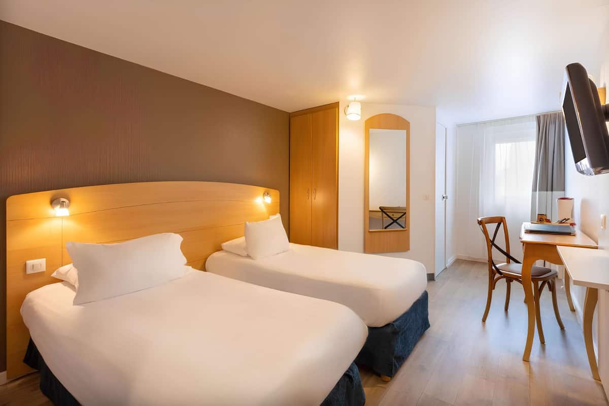 Una habitació d'hotel amb dos llits, un escriptori, una cadira, un mirall i un armari.