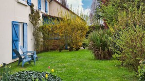 Un jardin avec un bâtiment blanc, des volets bleus et une chaise.