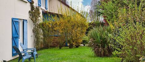 A garden with a white building, blue shutters, and a chair.