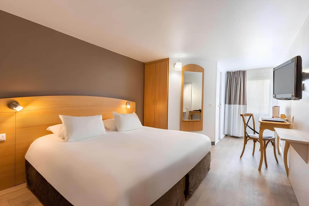 Habitació d'hotel amb un llit gran, una taula de treball, una cadira, un televisor i un mirall.