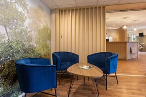 Ein Zimmer mit drei blauen Stühlen um einen Holztisch, einer Ziegelwand und einem Wandgemälde von Bäumen.