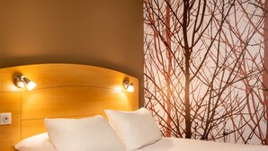 Une chambre d’hôtel avec une tête de lit en bois, deux oreillers blancs et un mur orné d’un motif représentant un arbre.