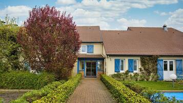 A two-story house with a tiled roof, a front entrance, and a swimming pool in the background.