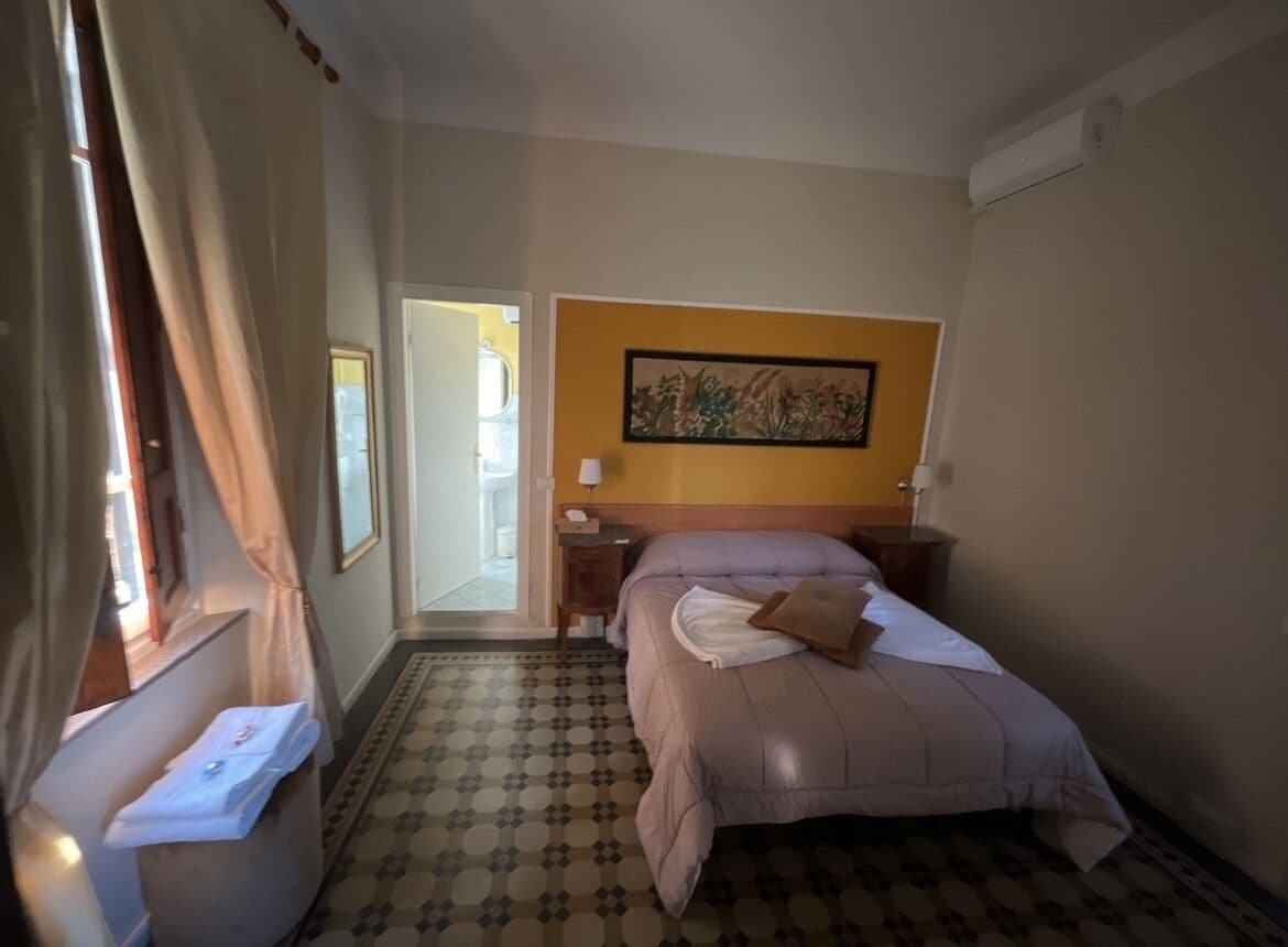 A hotel room with a bed, a nightstand, a lamp, a painting on the wall, and a patterned floor.